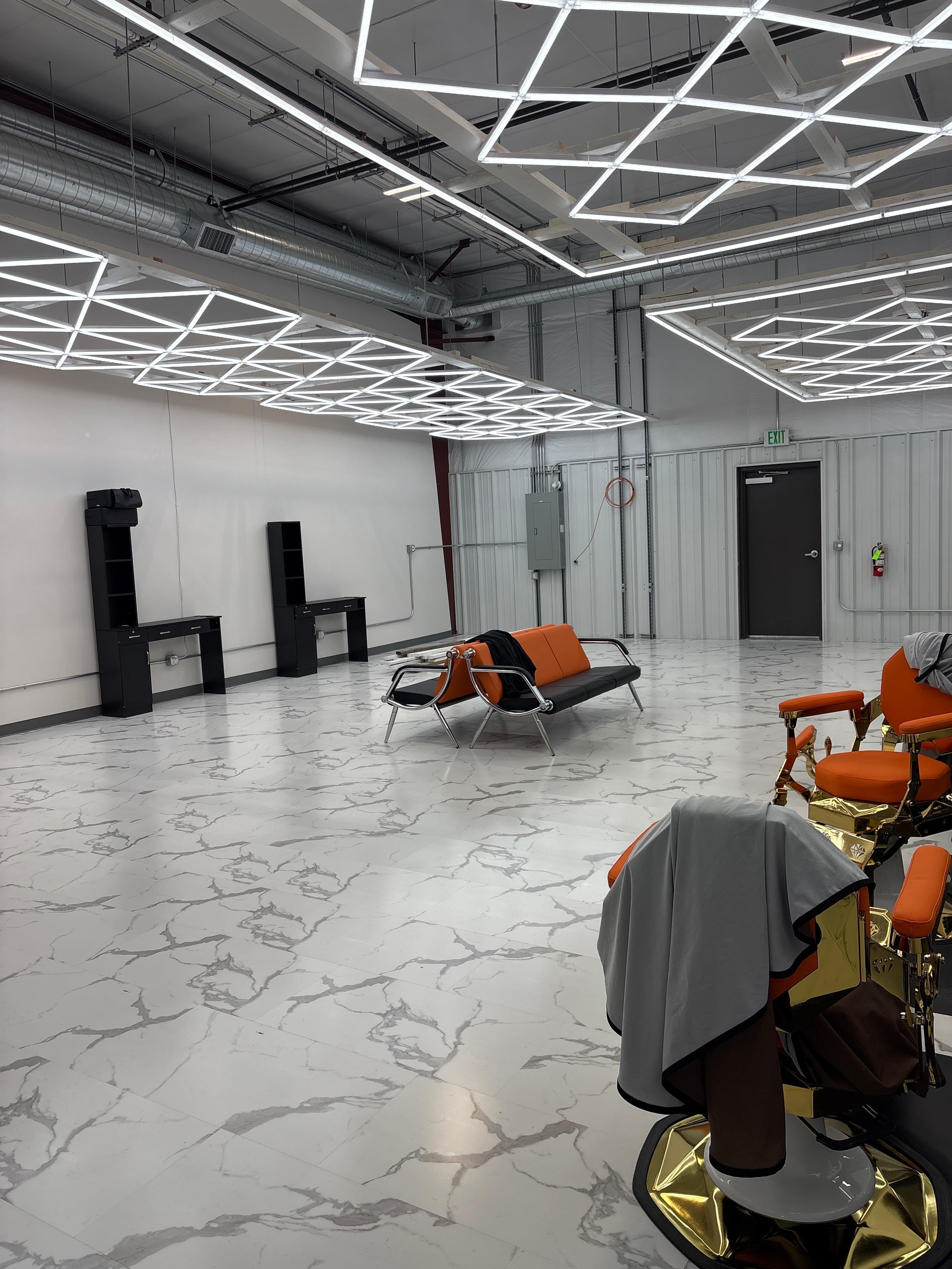 Wide view of the Clean Culture Barbershop #2 floor — orange barber chairs under a geometric LED ceiling grid, marble-look flooring