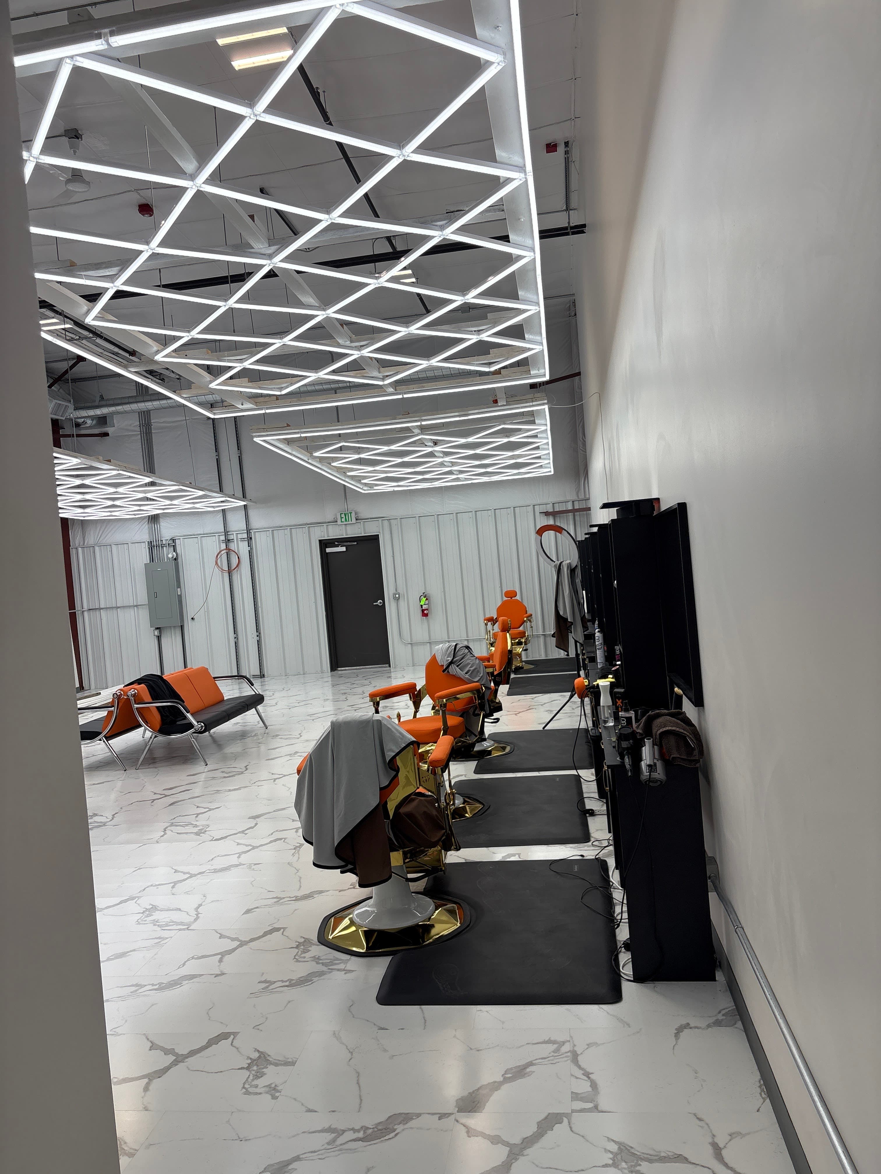Row of orange barber chairs lining the wall under the LED light grid at Clean Culture Barbershop #2